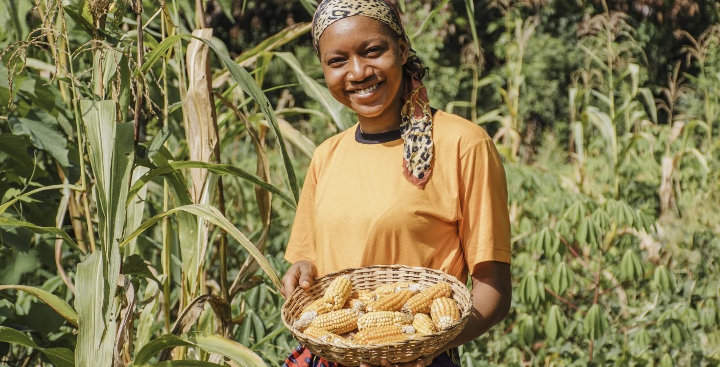 Agricultrice souriante portant un panier d'épis de maïs dans un champ de maïs