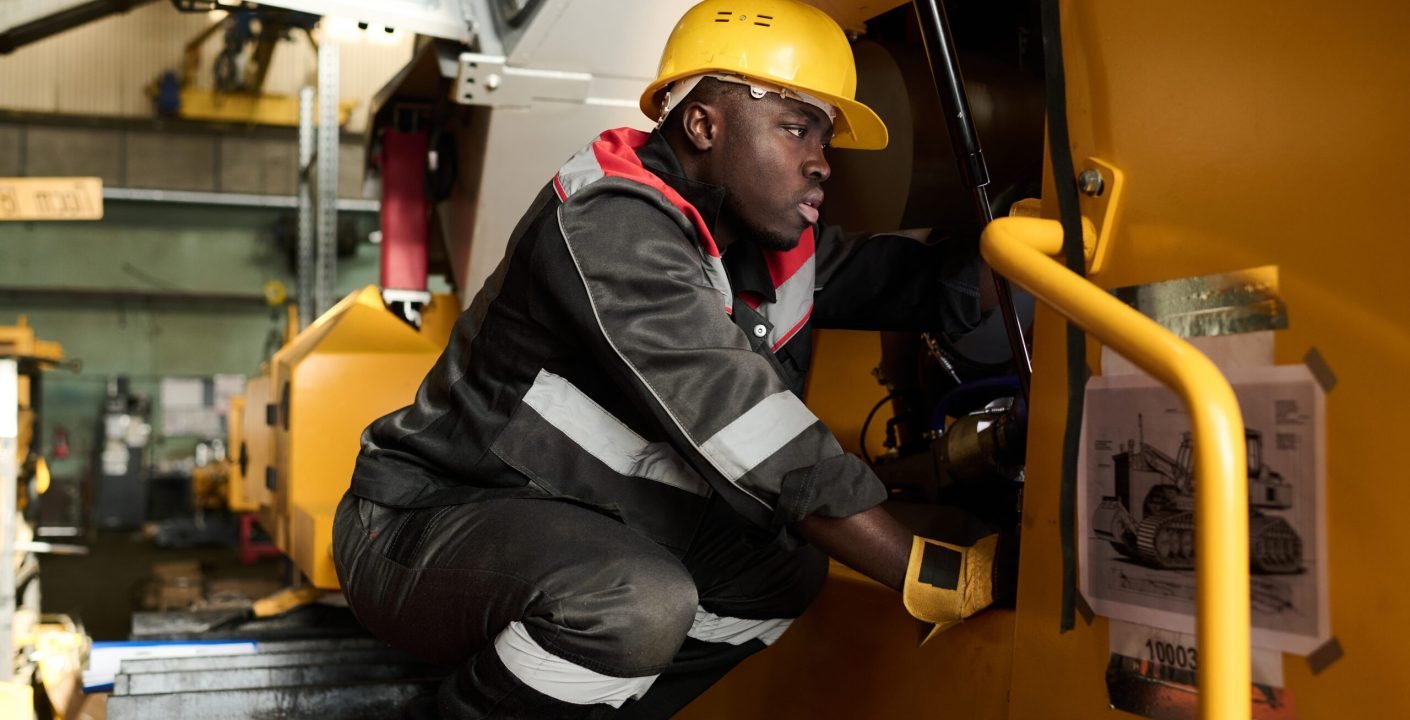 Technicien en casque de chantier vérifiant le mécanisme d'un engin lourd